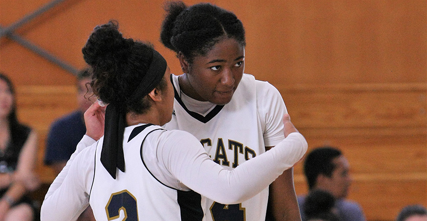 Two UC Merced women's basketball players discuss strategy during a game.