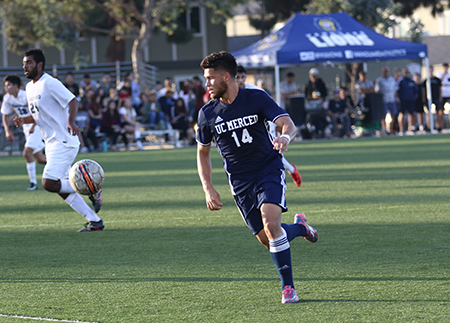 A UC Merced men's soccer player chases after the ball.