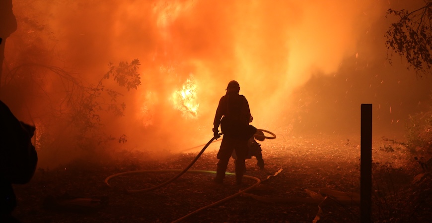 Photo depicts a silhouette of California firefighters battling a lightning-caused fire in 2020.