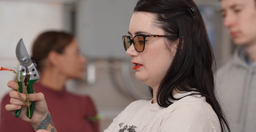 Photo depicts Ph.D. student Lynn Breithaupt holding up a native plant cutting.