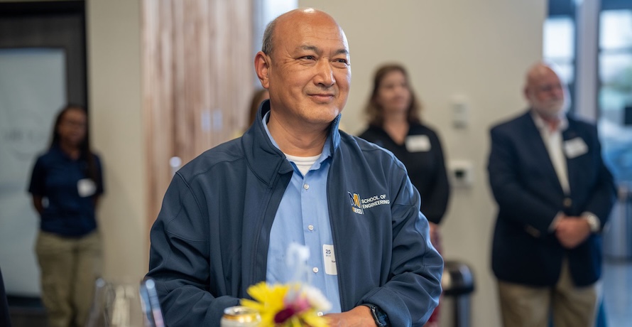Professor YangQuan Chen is pictured standing behind a table with flowers at UC Merced on Main.